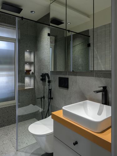 Grey terrazzo bathroom with vessel sink on mustard-edged counter and glass shower niche