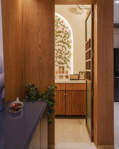 Wooden doorway opens to a pooja niche with painted floral arch and wood cabinetry