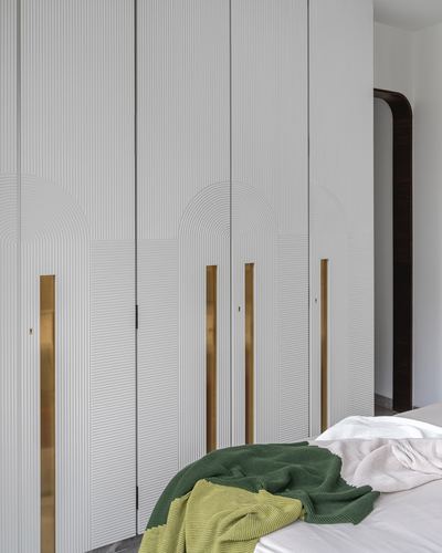 Fluted white wardrobe with arched detailing and brass handles beside a bed with green throws