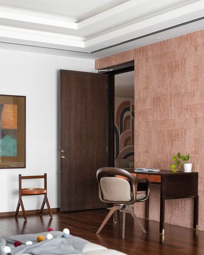 Study nook with wooden desk, cane chair, and textured terracotta wall beside an open dark door