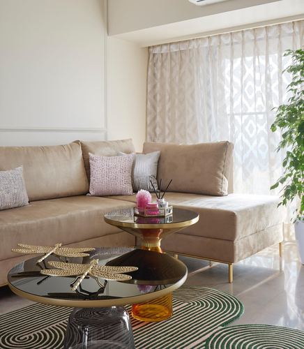 Beige sectional sofa with pastel cushions beside brass and glass round coffee tables