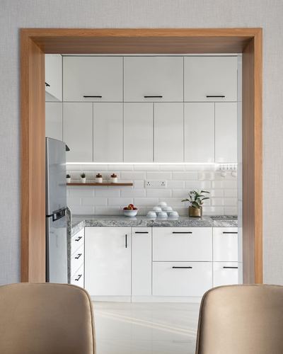 White modular kitchen framed by a wooden doorway, seen from dining area with two beige chairs