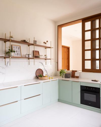 Mint green L-shaped kitchen with marble backsplash, open wood shelving, and a wooden sliding door beyond