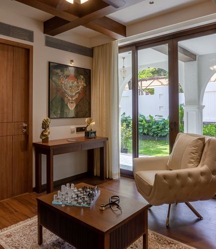 Living room with wooden beam ceiling, tufted armchair, console table and garden view through glass doors