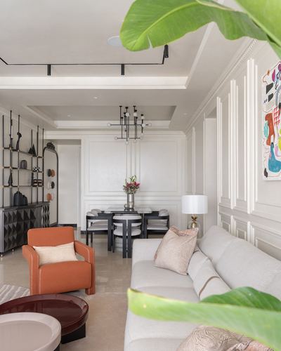 Living and dining area with orange armchair, beige sofa, panelled walls and black chandelier over dining table