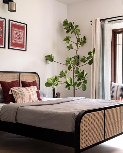 Bedroom with cane bed frame, red patterned wall art, and a tall potted plant by curtained window