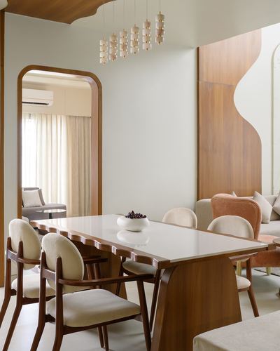 Dining room with scalloped wood table, boucle chairs, arched doorway and wavy wood panel wall