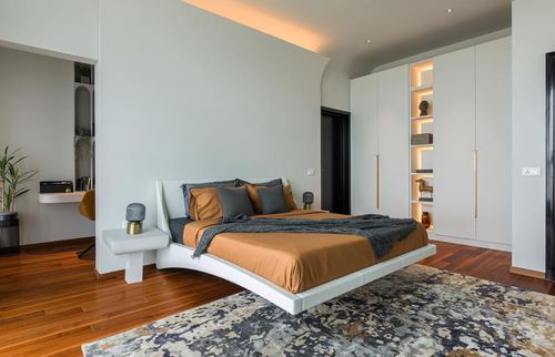 Modern bedroom with floating white bed, orange bedding, backlit built-in wardrobe niches
