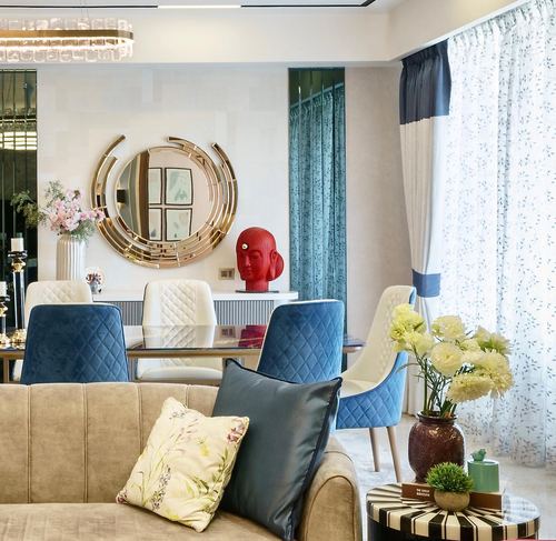 Living-dining space with navy quilted chairs, brass sunburst mirror, and red sculptural bust