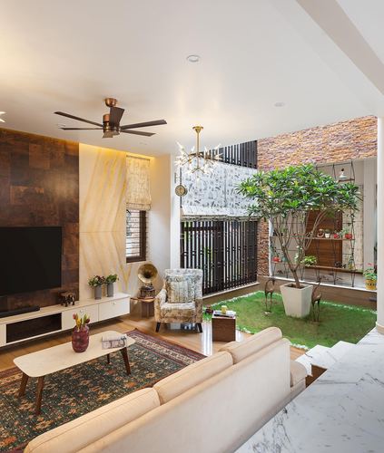 Living room with cream sofa, patterned armchair, and TV wall opening onto an interior courtyard with a tree