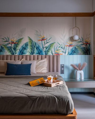Bedroom with tropical mural wallpaper, pink tufted headboard, and a tray of drinks on the bed