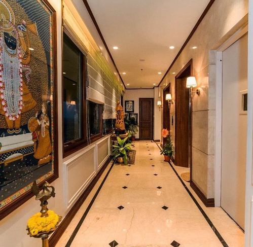 Long marble corridor in Kolkata home with pichwai painting, brass diya stand and warm sconce lighting