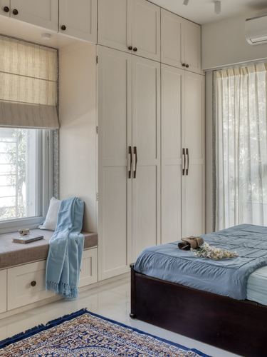 Bedroom with white wardrobe wall, window seat, and dark wood bed with blue linen