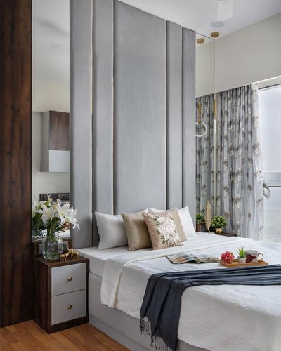 Bedroom with tall grey tufted headboard, floral sheer curtains, and walnut nightstand.