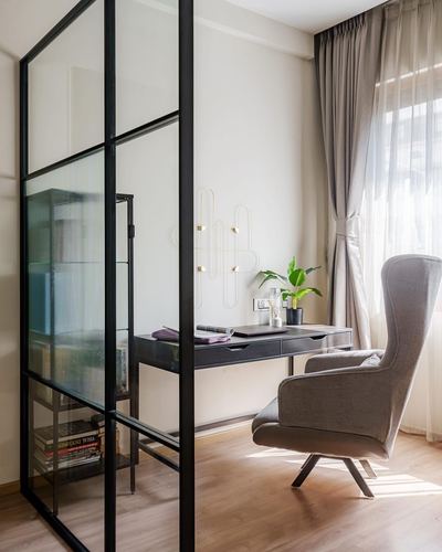 Study nook with wingback chair, black desk, and glass-framed partition beside curtained window