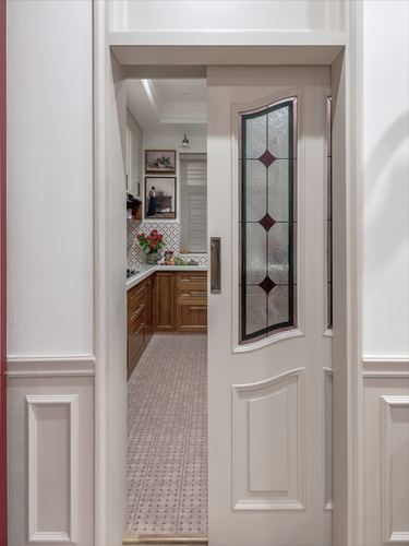 Open stained-glass pocket door revealing a wooden kitchen with patterned floor tiles beyond