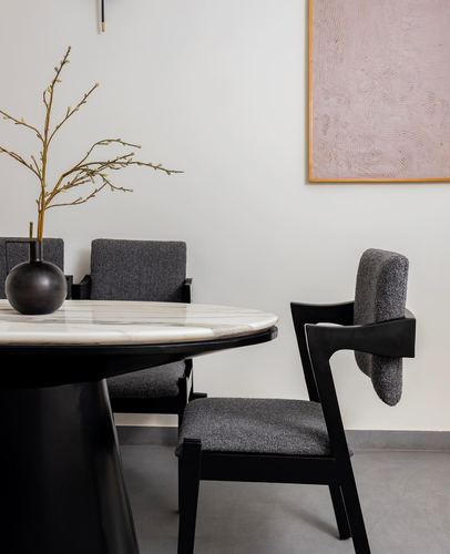Round marble-top dining table with black base and boucle chairs against neutral wall with pink artwork