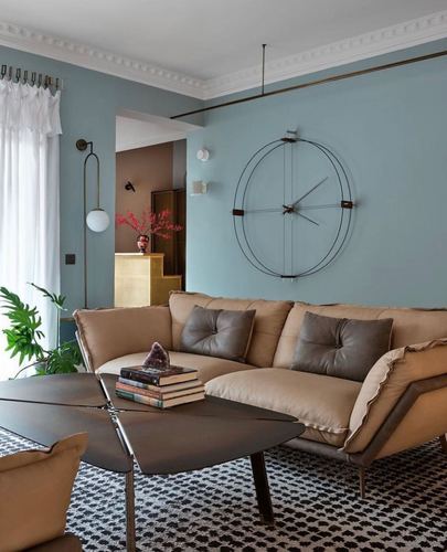 Blue-walled living room with tan leather sectional, large round wall clock, and patterned rug