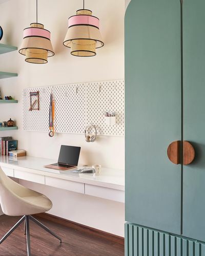 Study nook with cane pendant lights, white pegboard desk wall, and green arched cabinet door