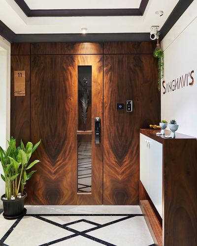 Wood-clad double entry doors with a lit niche, marble floor and Sanghavi's signage on wall