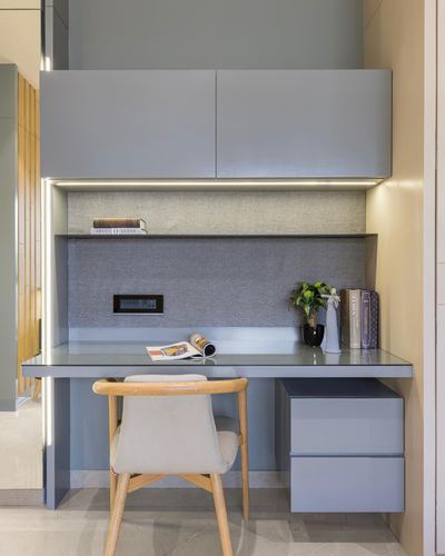 Built-in study desk with grey cabinetry, fabric backsplash panel and wooden chair
