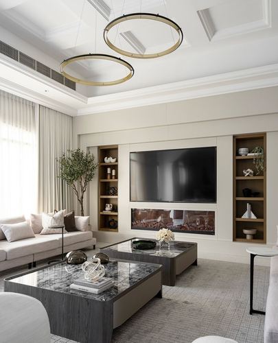 Neutral living room with built-in shelving, tv wall, fireplace, and two ring pendant lights above marble coffee tables