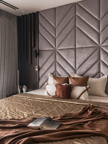 Bed with geometric tufted headboard, layered brown and cream bedding, textured wall panels behind