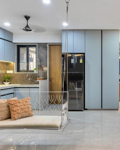 Pale blue kitchen with hanging acrylic swing, patterned cushions, and black refrigerator.