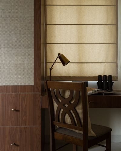 Wooden desk with cane-backed chair, brass lamp, and woven roman blind in study nook
