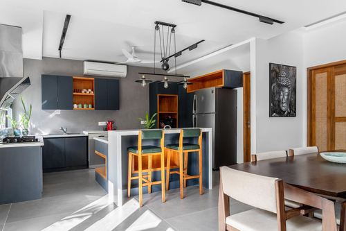 Open kitchen with navy cabinetry, orange shelf accents, and island with green-topped bar stools