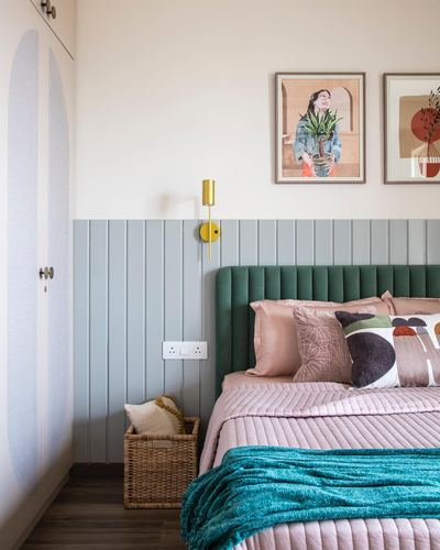Bedroom with green fluted velvet headboard, pink bedding, teal throw, and framed art above panelled wall