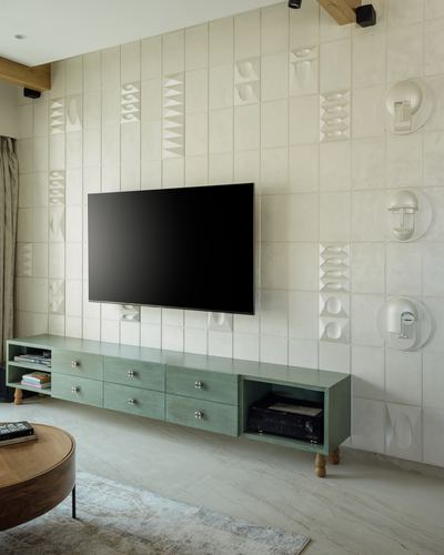 Sage green tv console against cream sculptural tile wall with round wall discs