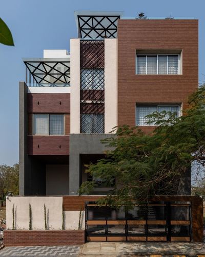 Three-storey Indore residence facade with brown stone cladding, jaali screen, and rooftop metal pergola