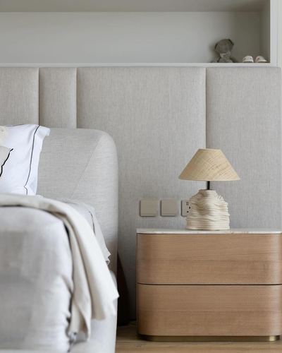 Beige channel-upholstered headboard bedroom with wood nightstand and woven-shade table lamp.