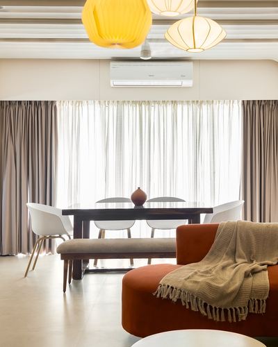 Living-dining space with terracotta sofa, wood dining table, and hanging pendant lights against sheer curtains