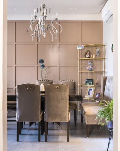 Dining table with velvet nailhead chairs beneath a crystal chandelier against a paneled mauve wall