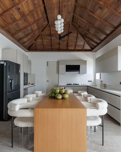 Open kitchen with vaulted wood ceiling, dining table, bouclé chairs, coconut centerpiece