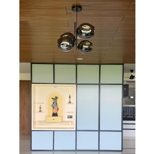 Pooja niche with arched recess set into a frosted glass and black-grid partition below a wooden ceiling with a chrome sputnik chandelier.
