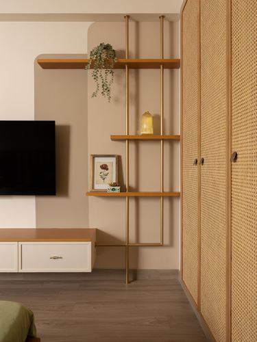 Living room corner with brass shelving, cane wardrobe, wall-mounted tv and arched niche in warm beige tones
