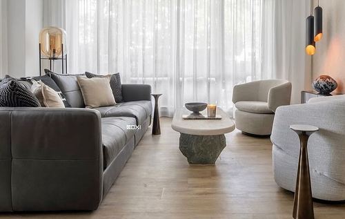 Grey leather sofa and cream armchair around a carved stone coffee table by sheer curtained windows