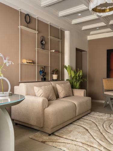 Beige living room with hanging shelves, taupe sofa, coffered ceiling and patterned rug