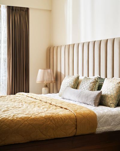 Bedroom with mustard quilted bedspread and channel-tufted beige headboard beside pleated lamp