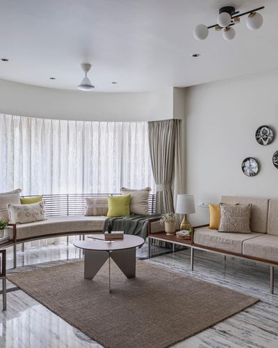 Curved living room with bay window seating, round wood coffee table and jute rug on marble floor