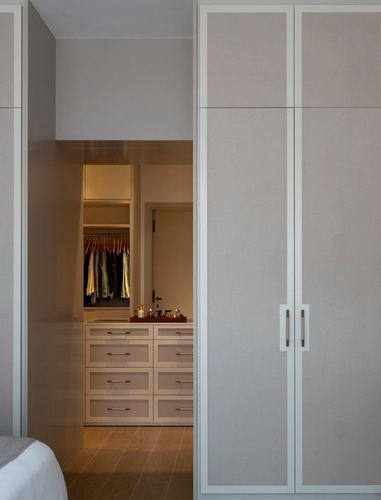 Bedroom with upholstered wardrobe doors and view through doorway into walk-in closet with drawers