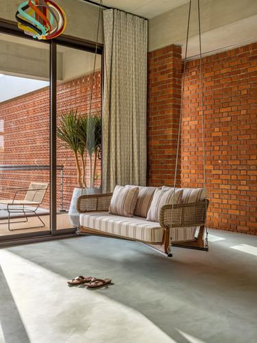 Cane swing sofa hangs before a brick wall in a sunlit living space with a slid-open glass door.