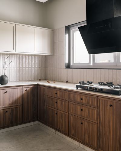 L-shaped kitchen with walnut-toned cabinetry, ribbed white backsplash, and angled black chimney hood over gas stove
