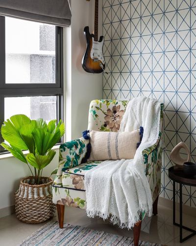 Floral wingback chair with white throw beside window, plant, and blue geometric wallpaper wall