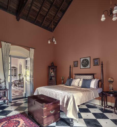 Terracotta-walled heritage bedroom with four-poster bed, vaulted wood ceiling, and black-white checkerboard floor