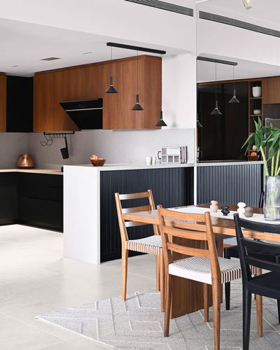 Open kitchen with wood cabinets and black fluted island, dining table with woven chairs in foreground
