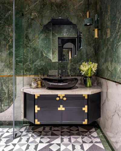 Corner bathroom vanity with black vessel sink under scalloped mirror against green marble walls